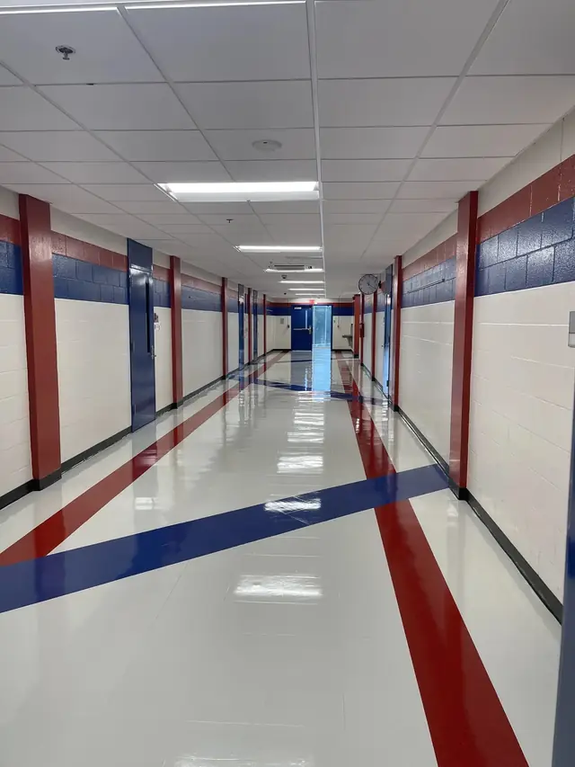A school corridor burnished to a gloss, blue and red stripes crossing the white vinyl under ceiling lights