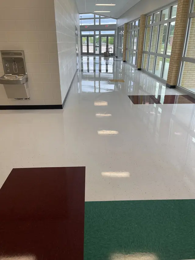 A long glossy school hall with tall windows down one side and a drinking fountain on the other