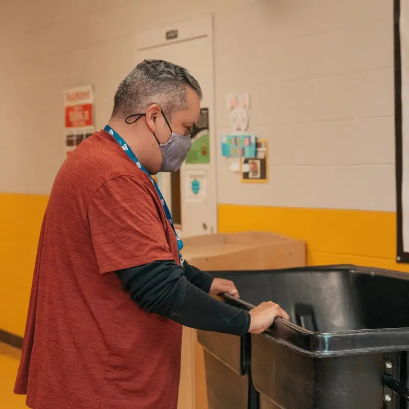 A ParCou team member in a face mask and lanyard emptying a bin in a school corridor