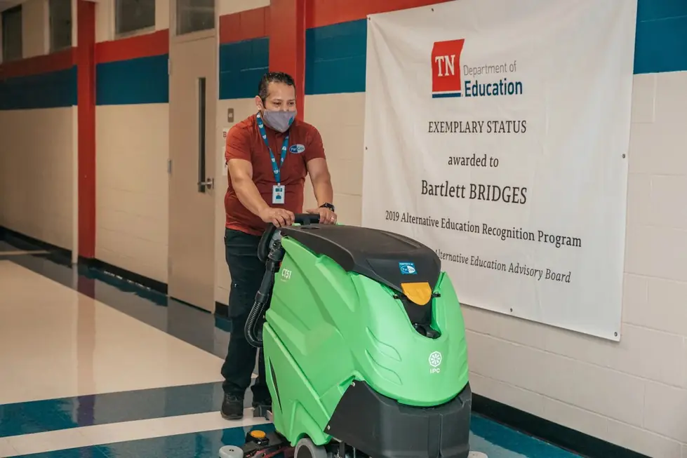 A ParCou team member running a green floor scrubber down a glossy school hall
