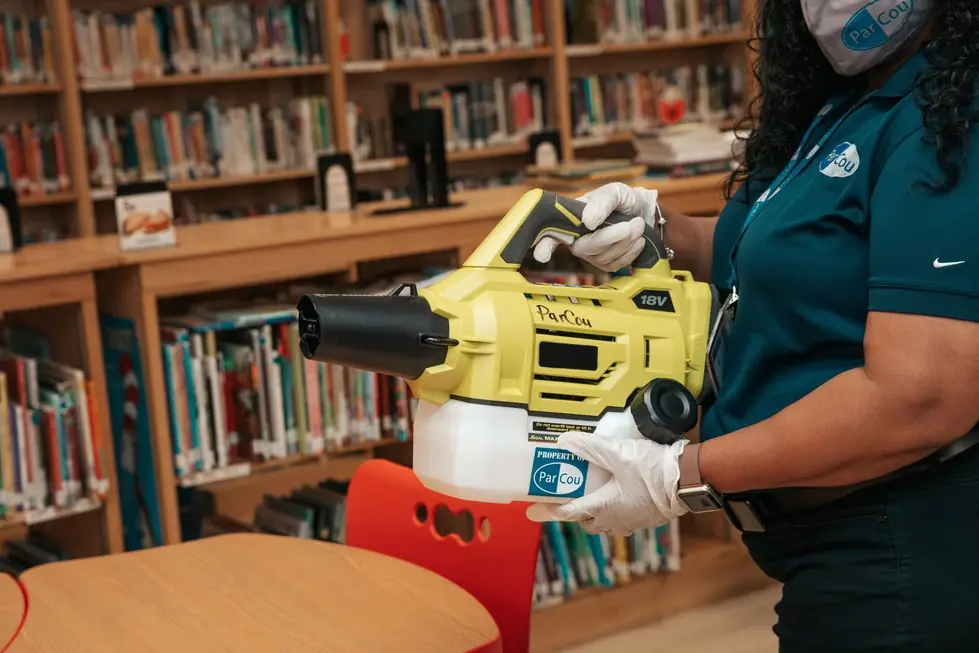 A ParCou team member in gloves and a face mask sanitizing a school library with a yellow fogger